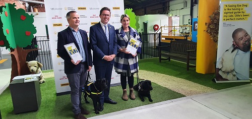 Two Seeing Eye Dog handlers stand with their dogs, with another man between them