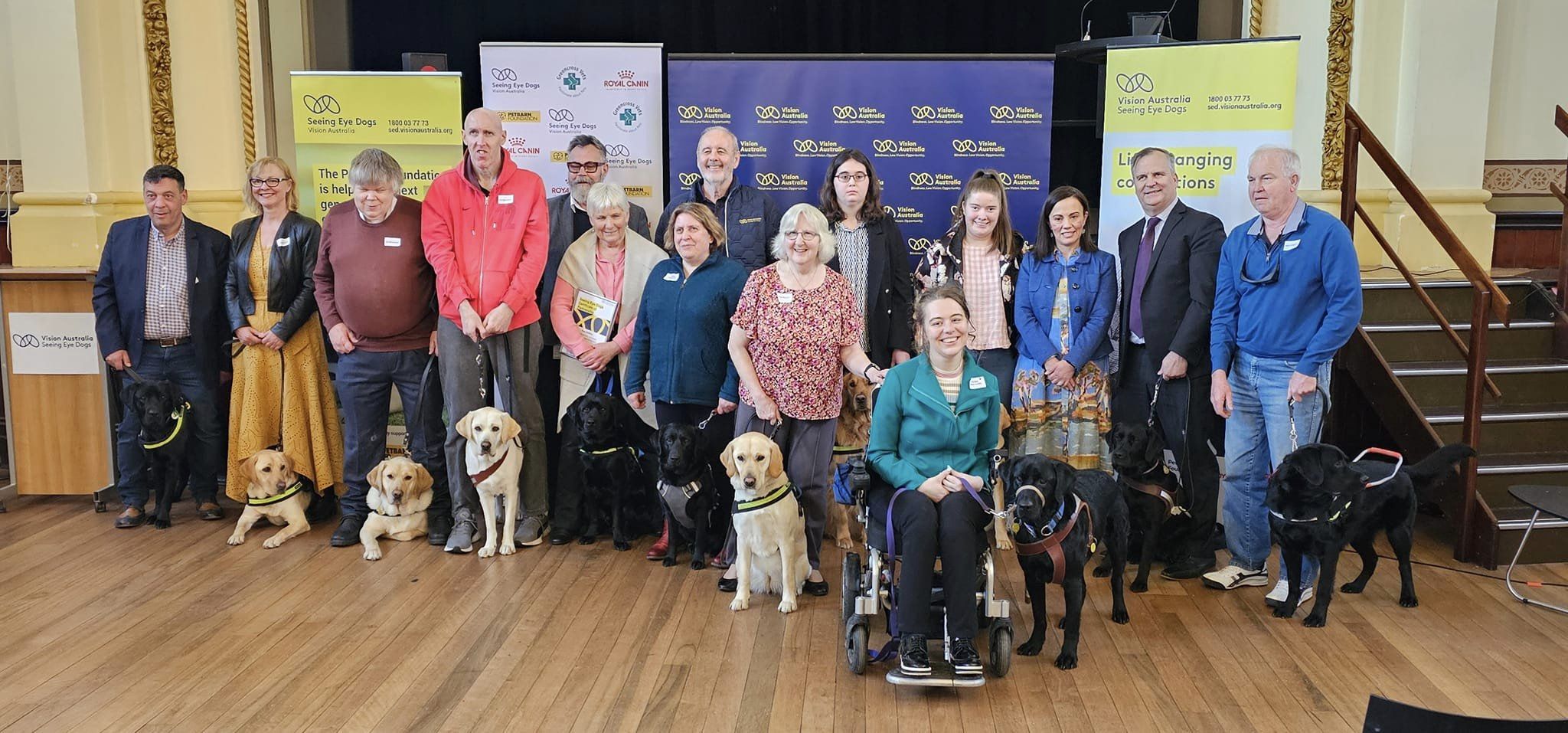 "A group of people and Seeing Eye Dogs stand in front of a stage"