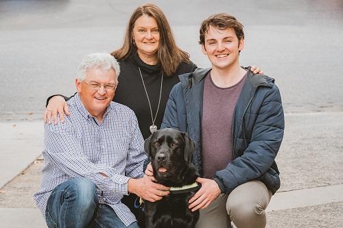 Two men and a women kneel with a black labrador