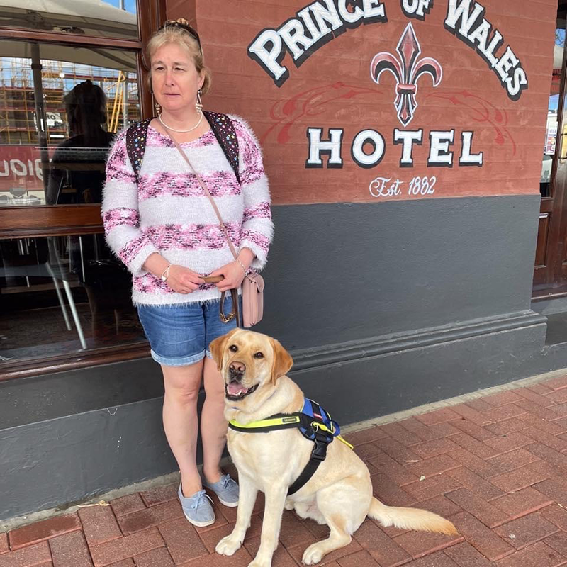 Lynn stands next to Seeing Eye Dog Hector, in harness.