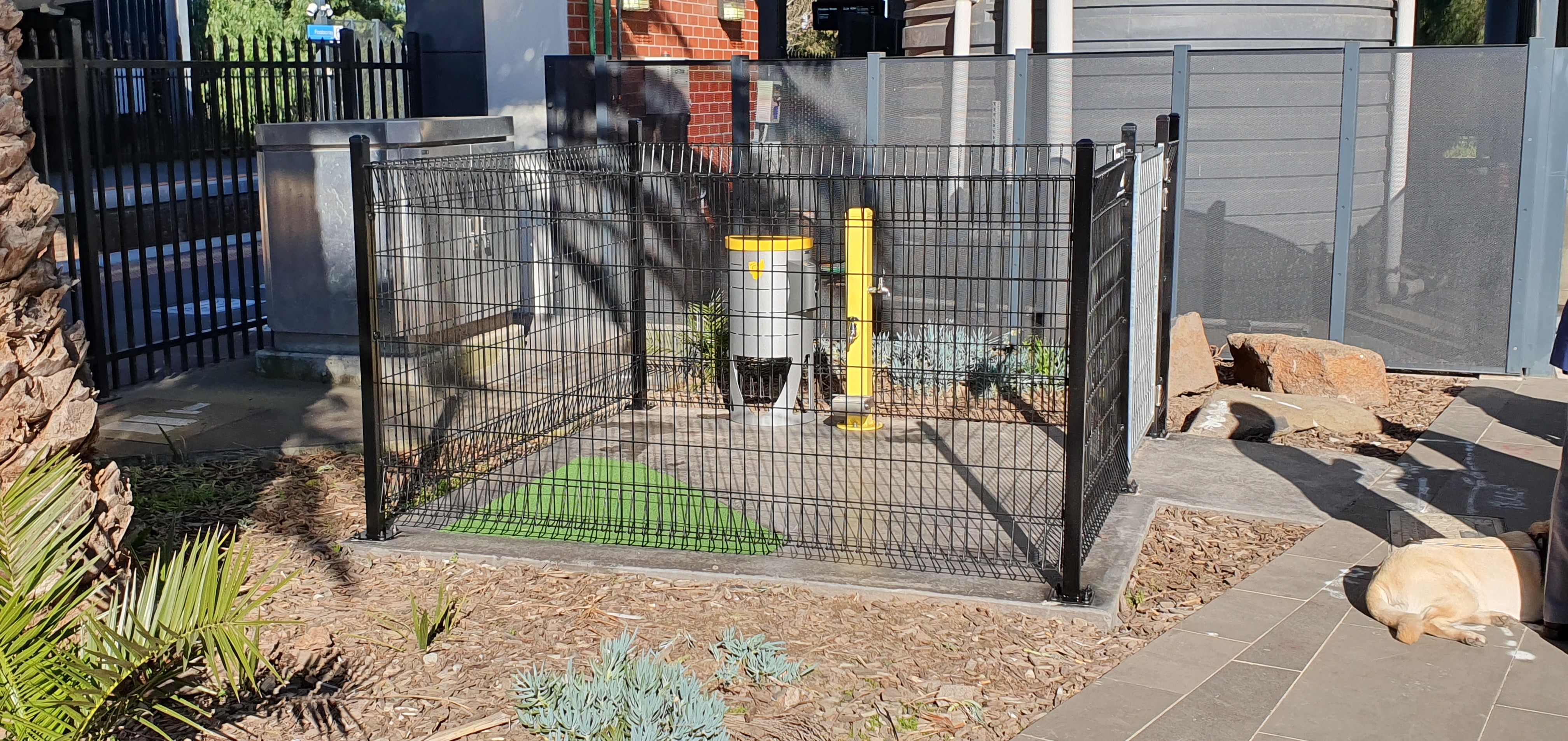 The Assistance Animal Relief Area at Footscray Station, complete with grassy area, a lidded bin and a plastic bag dispenser.