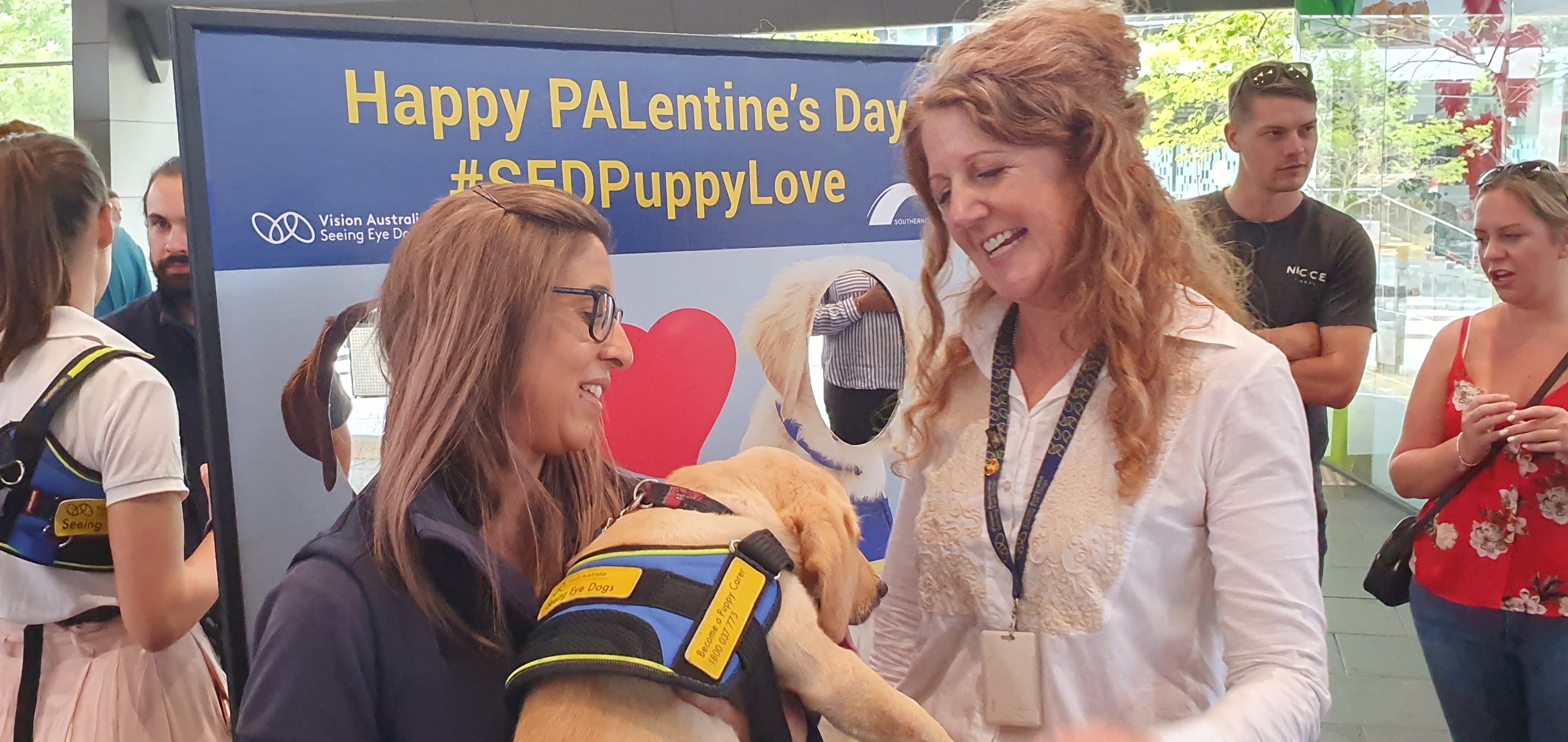 SED Staff Kim and Jane standing in front of our Dog Standee, Kim has a younger golden SED in her arms