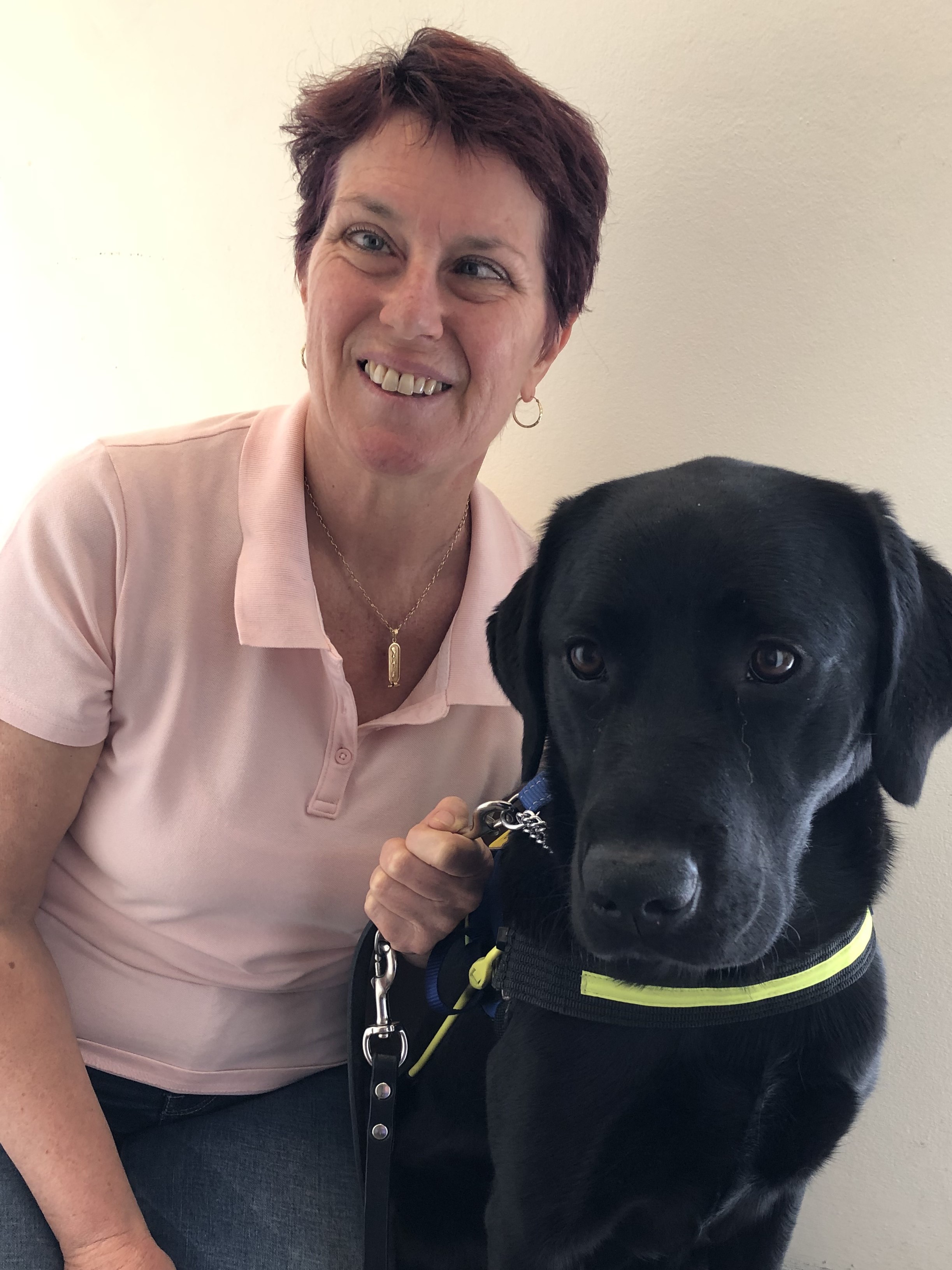 Eleni in a pink shirt crouches down next to black Seeing Eye Dog Laura