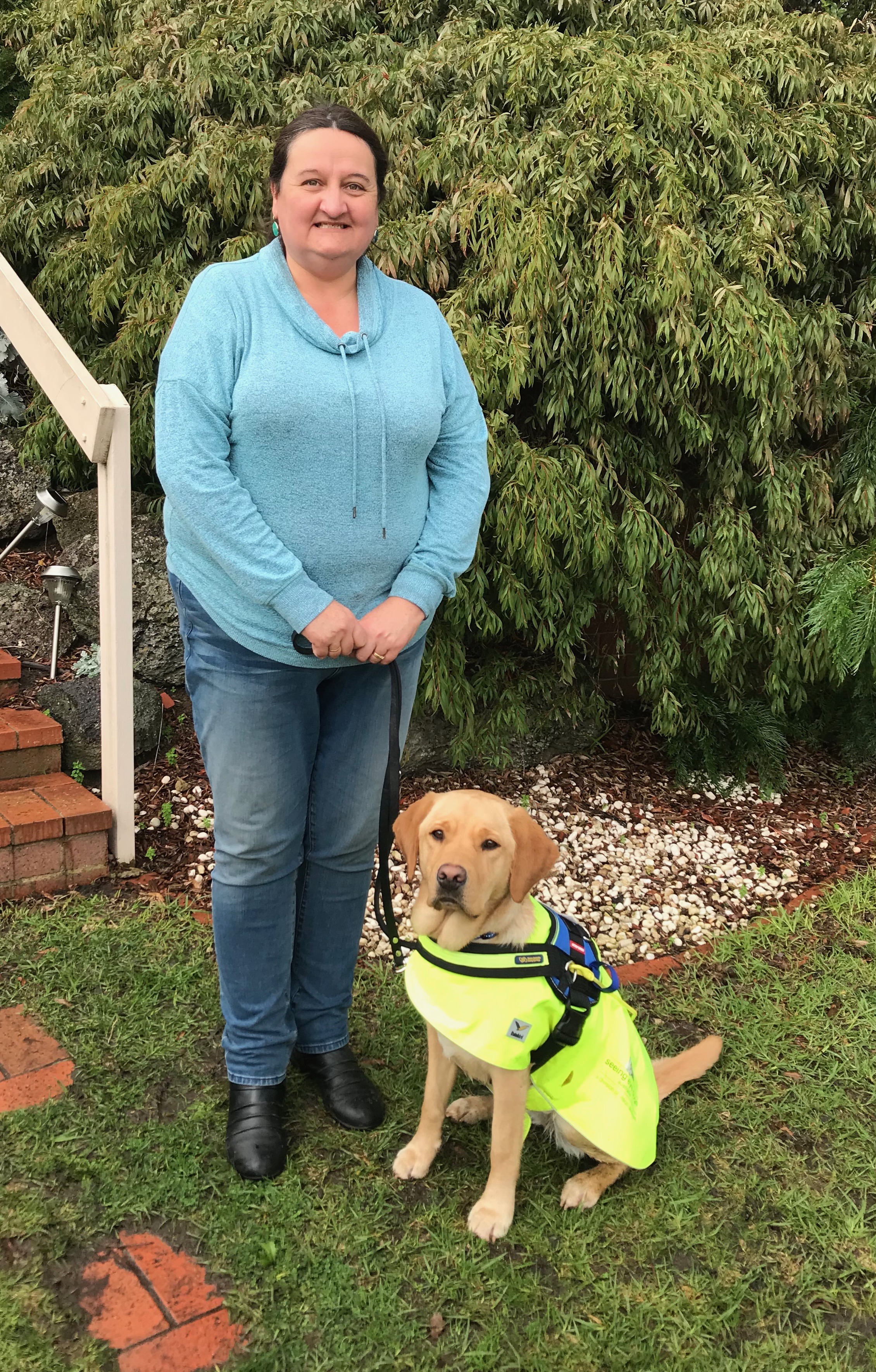 Kim and her Seeing eye Dog Raya stand outside a house.