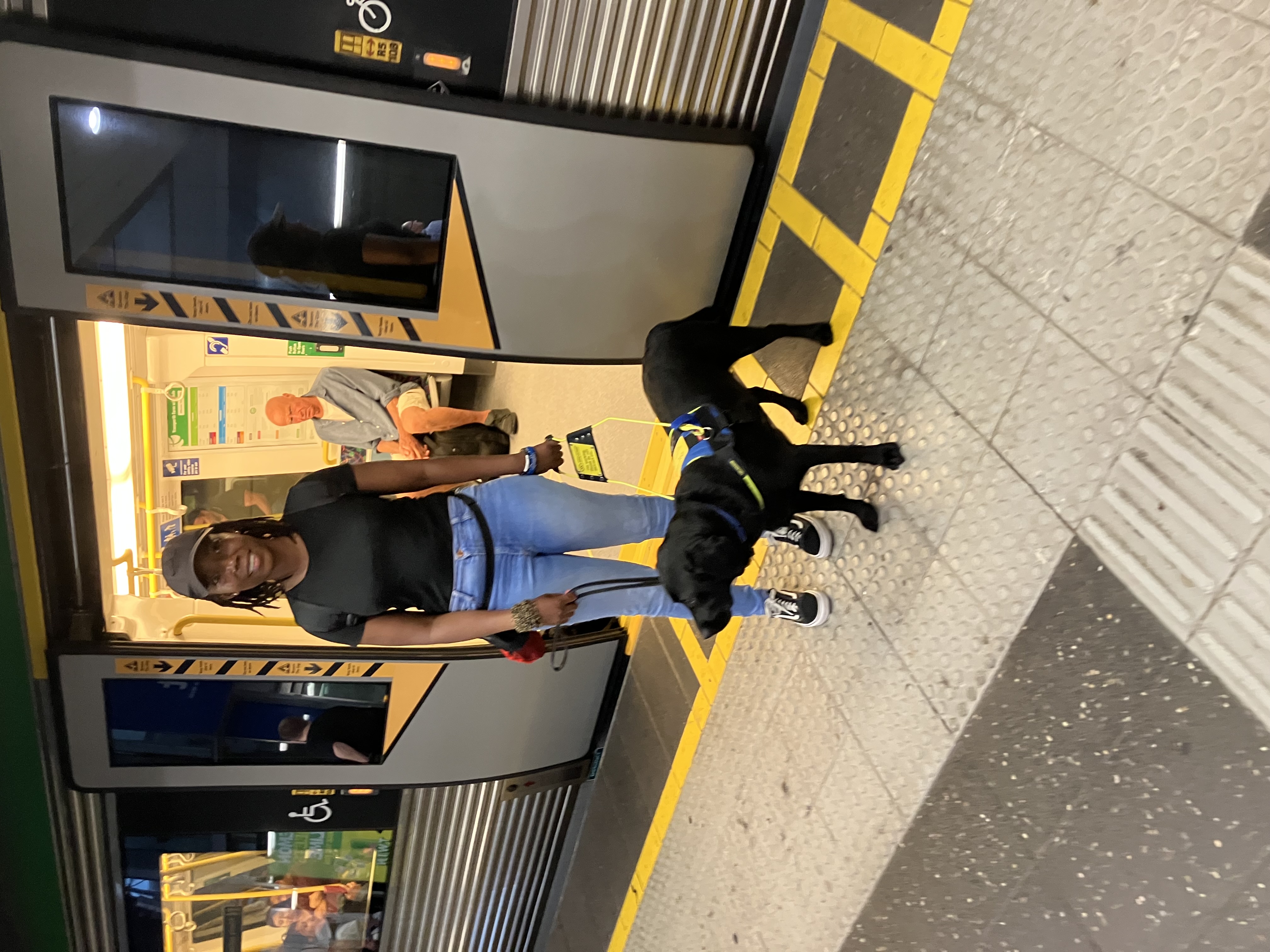 Thayana and Seeing eye dog Shaylah standing in front of a train with an open door, Thayana is smiling.